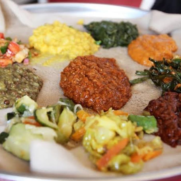 A beyaynetu combination platter of lentil, split pea, cabbage, collard green and salad dishes spread over injera