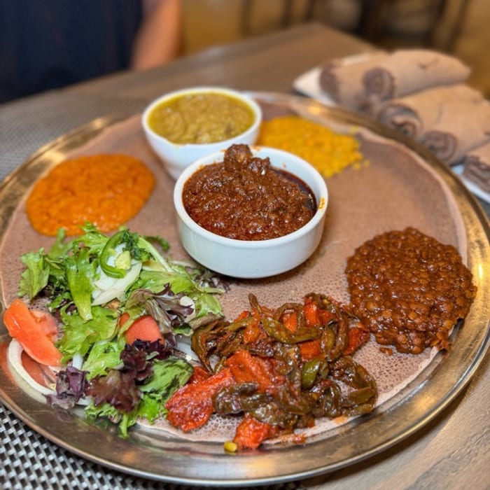 A silver tray of injera with misir wat, shiro, kik alicha, tibs, salad and rolled injera on the side