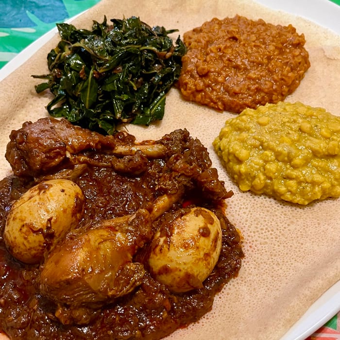 Doro wat with hard-boiled eggs and chicken served on injera with collard greens, split pea stew and lentils