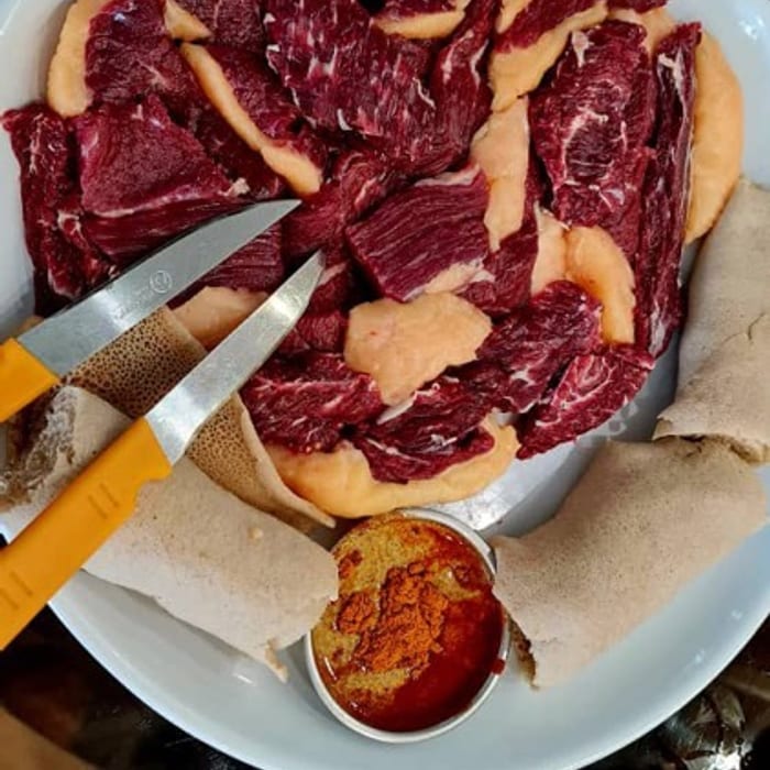 Freshly cut raw beef arranged on injera with a carving knife and a dish of mitmita